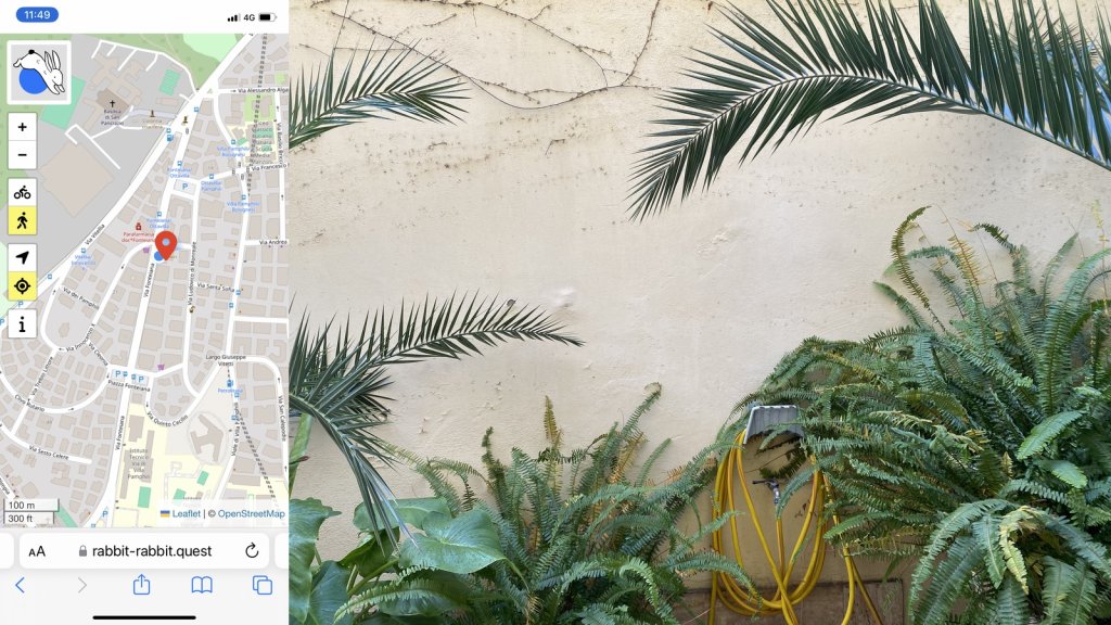 Composite image. On the left a map showing the location of the quest and my position. On the right, a pale cream coloured wall with some palm fronds intruding from left and right and ferms and a colocasia on the bottom. There is a yelloqw hosepipe coiled up on the wall.