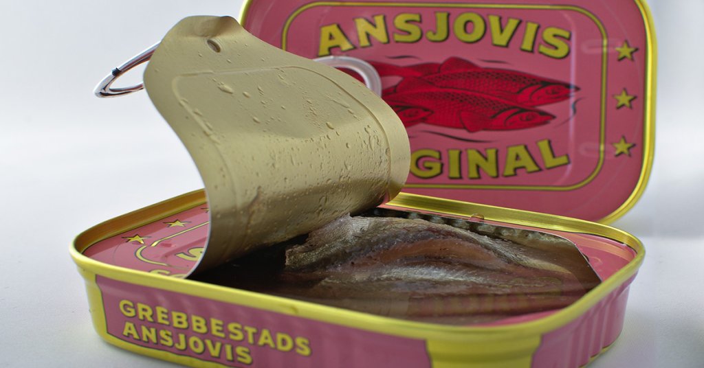 A tin of Swedish ansjovis with the lid half open showing the silvery fish within. The background is an unopened tin, prink with yellow lettering and two red fish on it.